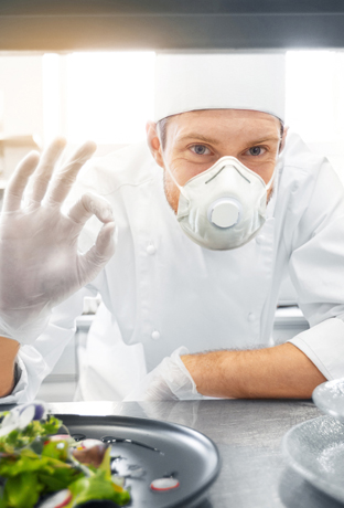 Male chef in mask with food at restaurant kitchen
